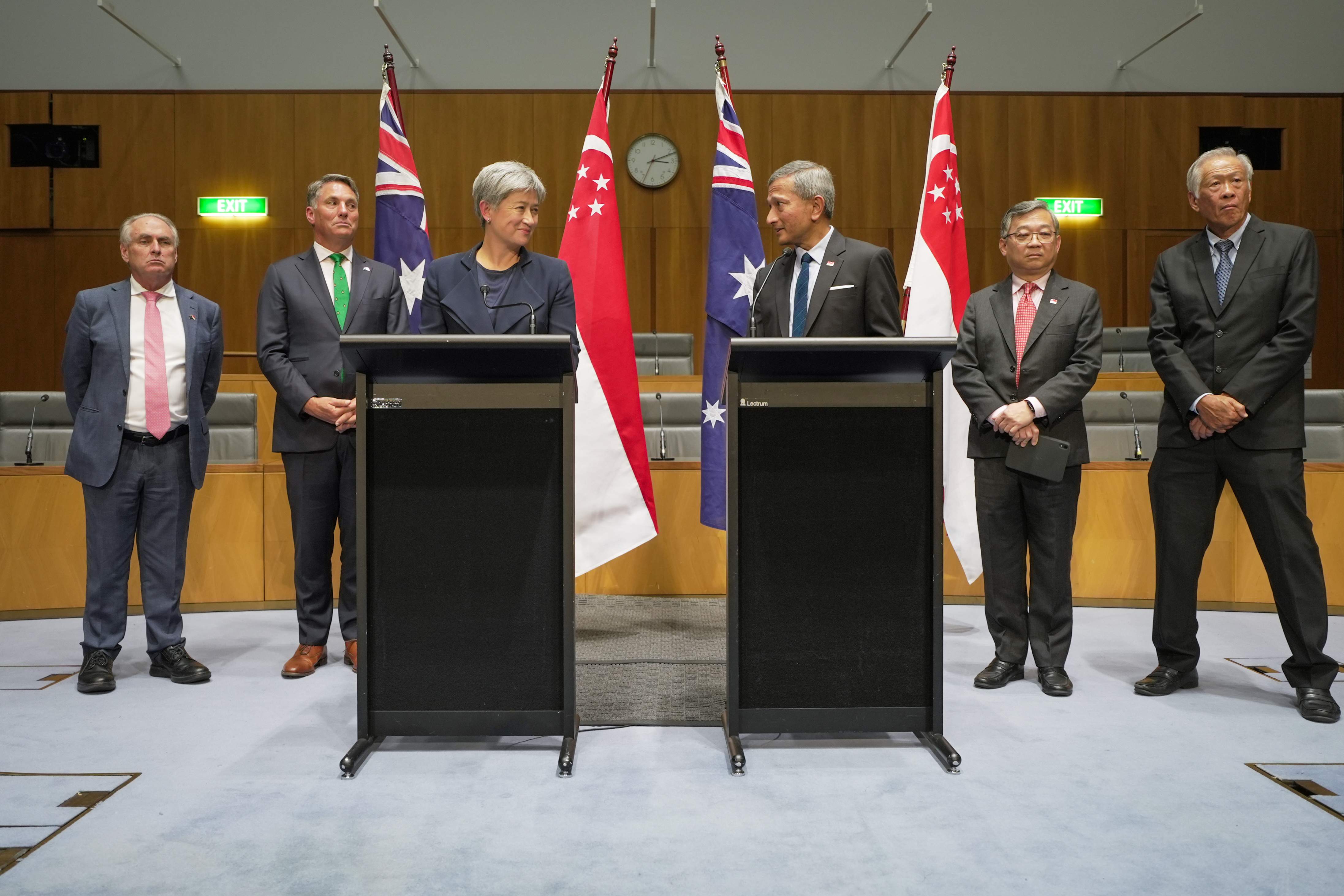 Six people behind two lecterns with Australian and Singaporean flags.